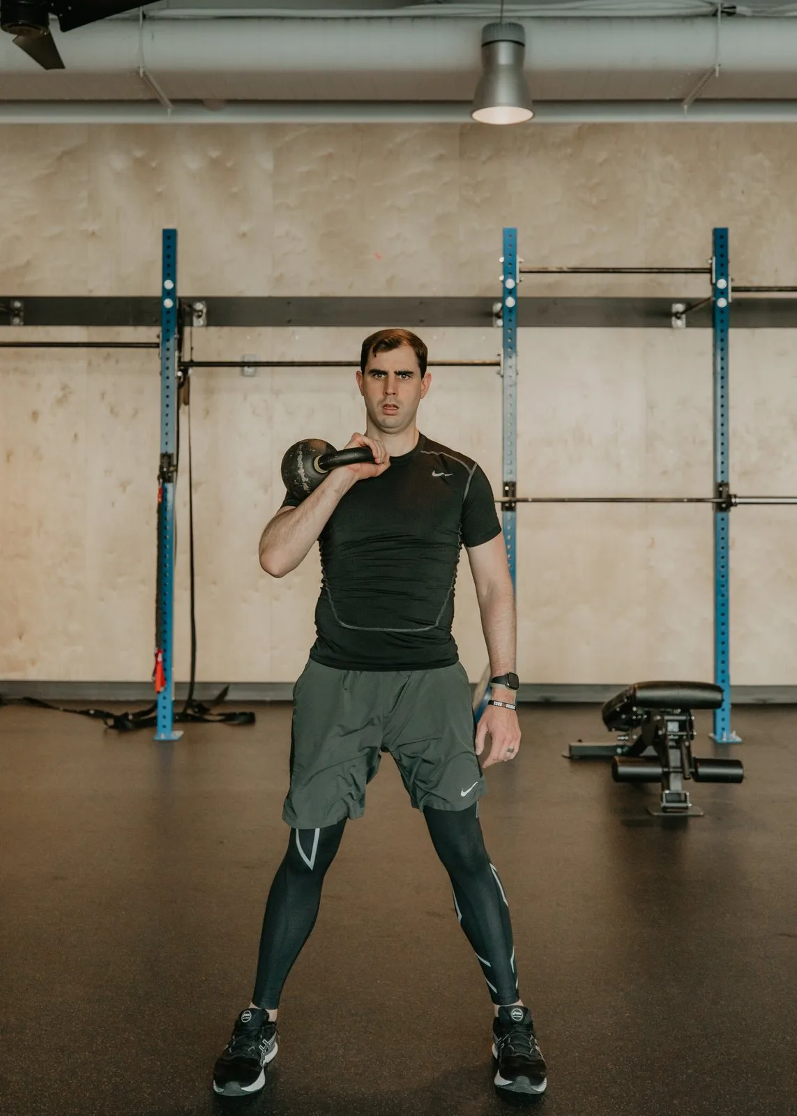 Nathan Brennan holding a kettlebell at the rack position in front of a squat rack